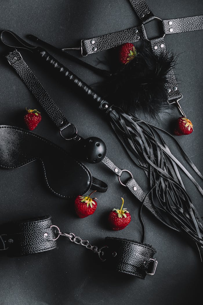 Black leather BDSM accessories with strawberries on a dark background. Captivating and intriguing composition.